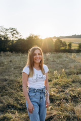 Beautiful happy smiling woman staying in the field at sunset