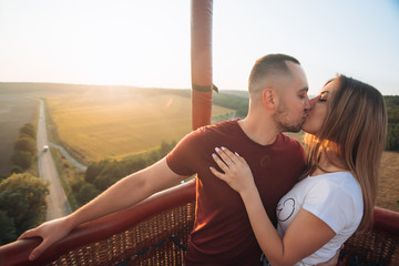 Beautiful attractive smiling couple staying and kissing in air baloon basket at sunset. Couple first time on baloon flight