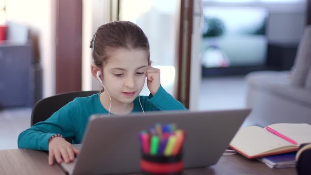 Little girl studying with laptop pc. Young female student learning with computer. Busy child doing school homework and e-learning during Covid-19 quarantine. Remote education at home