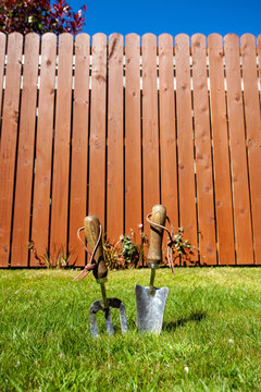 Garden hand fork and trowel on grass against a wood fence under a blue sky