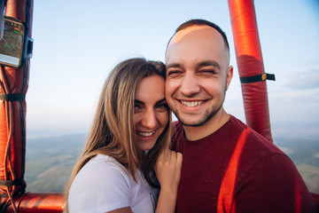 Happy smiling couple staying in air baloon basket at sunset. Couple first time on baloon flight