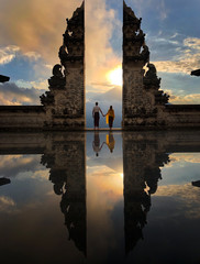 Happy young couple staying in temple gates of heaven and holding hands of each other. Lovers looking at the sunset. Perfect Honeymoon concept. Lempuyang Luhur temple in Bali, Indonesia. © Andrii