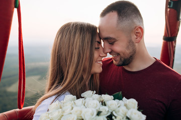 Handsome man with his beautiful girlfriend in air balloon flight. Romantic photo of lovely couple in baloon basket at sunset. Original proposal of marriage