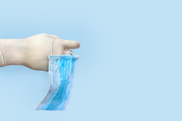 Blue disposable breath mask on hand in medical gloves on the blue background with space for text....