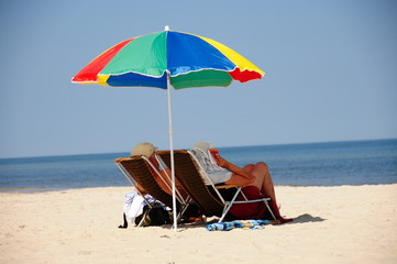 Urlop, wakacje, odpoczynek i relaks na plaży w cieniu parasola na leżaku, pan i pani na urlopie - obrazy, fototapety, plakaty