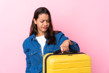 Traveler Colombian woman holding a suitcase over isolated pink background with sad expression