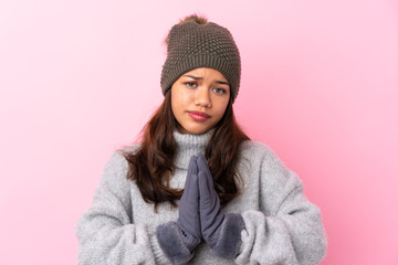 Young Colombian girl with winter hat over isolated pink wall pleading