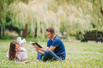 Young romantic couple lying in park and reading books