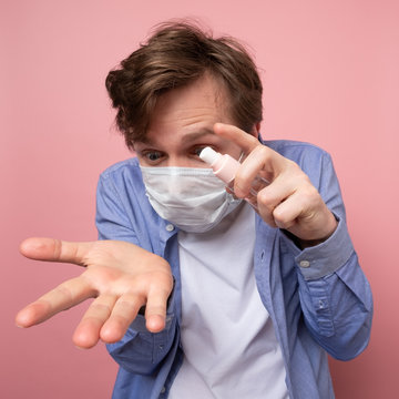 Caucasian man in medical mask spraying sanitizer spray over pink background