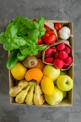 Donation box with fresh organic fruits, vegetables and herbs on a concrete background. Proper nutrition. Delivery healthy food to the home. Vertical, top view.