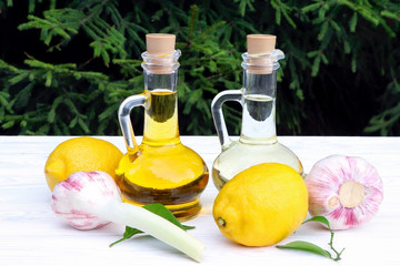 Olive oil and sunflower oil in decanter on a white wooden table. Limons, orange and garlic on a...