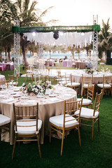 International Wedding outdoor celebration party under palm trees. Served tables on green area in hotel. Landyard. Beige and pink colors. Close-up and wide angle. - 341813181