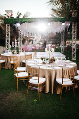 Fototapeta na wymiar International Wedding outdoor celebration party under palm trees. Served tables on green area in hotel. Landyard. Beige and pink colors. Close-up and wide angle.