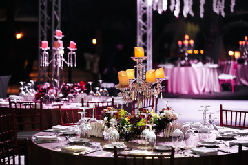 International Wedding outdoor celebration EVENING party under palm trees. Served tables on green area in hotel. Landyard. Beige and pink colors. Candles stand on tables - 341813537