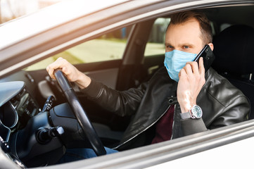 A young man is wear surgery mask on his face in a car. He is talking phone. Coronavirus pandemia, epidemia covid-19