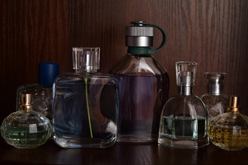 Glass bottles of perfumes of different sizes on the background of dark wooden shelf.