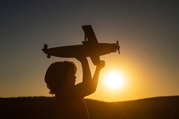 Fototapeta na wymiar Child pilot aviator with toy airplane dreams of traveling in summer in nature at sunset.