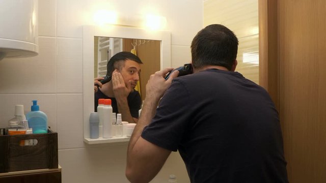 Man hair cutting himself with hair trimmer in bathroom