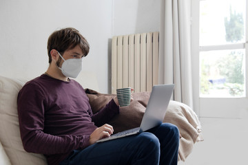 man working on his computer from the couch with a face mask