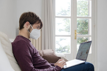 man working on his computer from the couch with a face mask