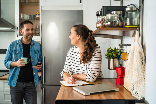 Young Man and Woman Couple talking and making the shopping list in their kitchen at home. Working at home and staying at home.