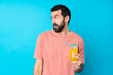 Young man over holding a cocktail over isolated blue background making doubts gesture looking side