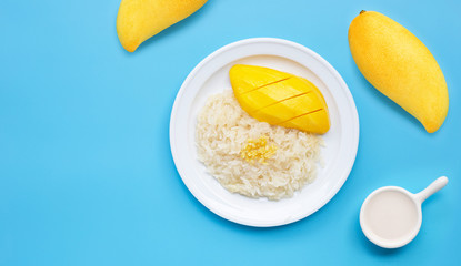 Thai dessert, sweet sticky rice with mango and coconut milk on blue background.