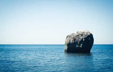 A lone large boulder stands in the middle of the sea. Blue ocean. Black Sea. Summer seascape.