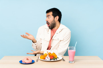 Man at a table having breakfast waffles and a milkshake with surprise facial expression