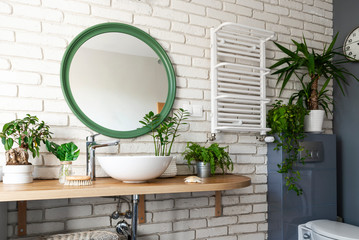 Interior of white bathroom with green plants, brick wall, wooden counter, ceramic washbasin and...