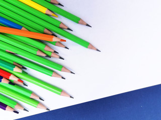Fototapeta premium multi-colored pencils among ordinary pencils from a corner lie on white paper