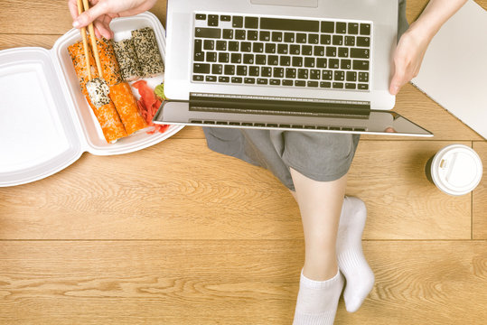 Takeout Box With Sushi On The Floor. Woman Eating And Working With Laptop, Phone, And Meals. Copy Space For You Text