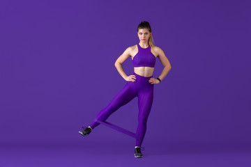 Fototapeta na wymiar Strong. Beautiful young female athlete practicing in studio, monochrome purple portrait. Sportive caucasian fit model with elastics. Body building, healthy lifestyle, beauty and action concept.