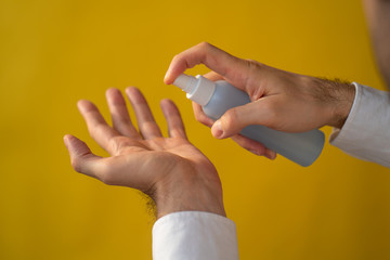 man's hand holds bottle of blue hand sanitizer spray on yellow background. Hand hygiene. Bacteria and virus protection