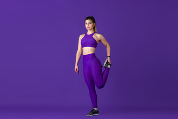 Fototapeta na wymiar Stretching. Beautiful young female athlete practicing in studio, monochrome purple portrait. Sportive caucasian fit model training. Body building, healthy lifestyle, beauty and action concept.