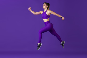 Fototapeta na wymiar In jump. Beautiful young female athlete practicing in studio, monochrome purple portrait. Sportive caucasian fit model training. Body building, healthy lifestyle, beauty and action concept.