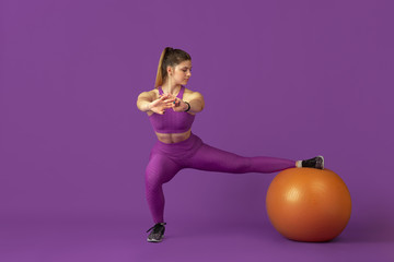 Shape. Beautiful young female athlete practicing in studio, monochrome purple portrait. Sportive caucasian fit model training with fitball. Body building, healthy lifestyle, beauty and action concept.