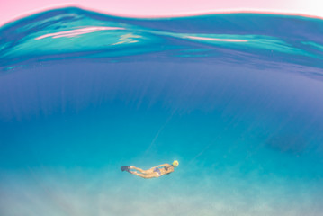 Woman in bikini swimming underwater over sand in blue ocean