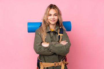 Teenager Russian mountaineer girl with a big backpack isolated on pink background keeping the arms...