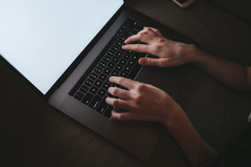 Woman is typing on a laptop keyboard while lying on a sofa at home in the dark. White laptop screen