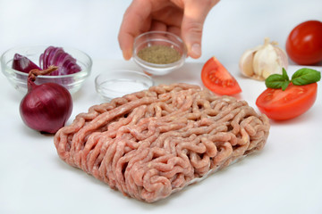 raw minced meat and vegetables and cook's hand on a white background on the kitchen 