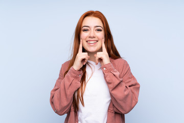 Redhead teenager girl over isolated blue background smiling with a happy and pleasant expression