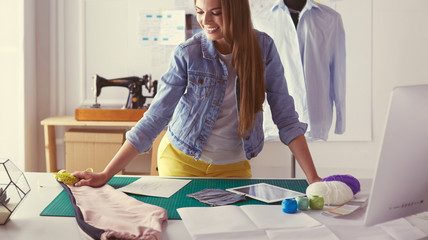 Beautiful fashion designer standing near desk in studio