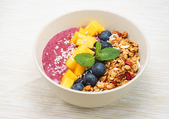 Handmade Bowl healthy tasty breakfast of yogurt, smoothie with granola, nuts, mango and berries.