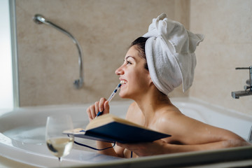 Excited woman enjoying relaxing bath at home.Spa self care night.Inspired creative person writing gratitude diary/journal.Resolution list.Making plans.Writing thoughts and ideas.Motivation.Life change