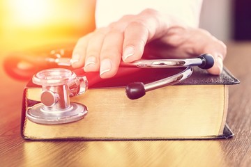 Doctor's hand with stethoscope on top of an old book