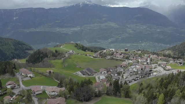 Aerial view of improbable green meadows of Italian Alps, green slopes of the mountains, Bolzano, huge clouds over a valley, roof tops of houses, Dolomites on background, sunshines through clouds