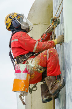 Working at height. Closed up abseiler wearing Personal Protective Equipment (PPE) climbing at the edge of oil and gas platform for touch up painting on pipeline.
