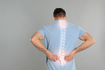 Man suffering from pain in spine on grey background - obrazy, fototapety, plakaty