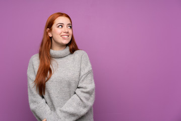 Fototapeta premium Redhead teenager girl over isolated purple background laughing and looking up